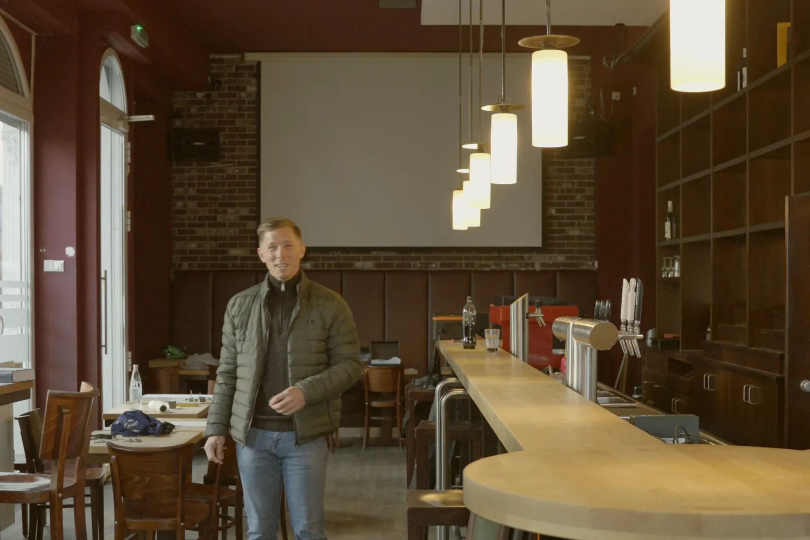 Gastraum mit großer Leinwand, Pendelleuchten und der langen Theke